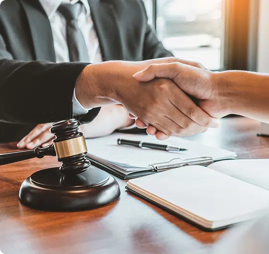 Two people shaking hands at a desk, with a gavel on it